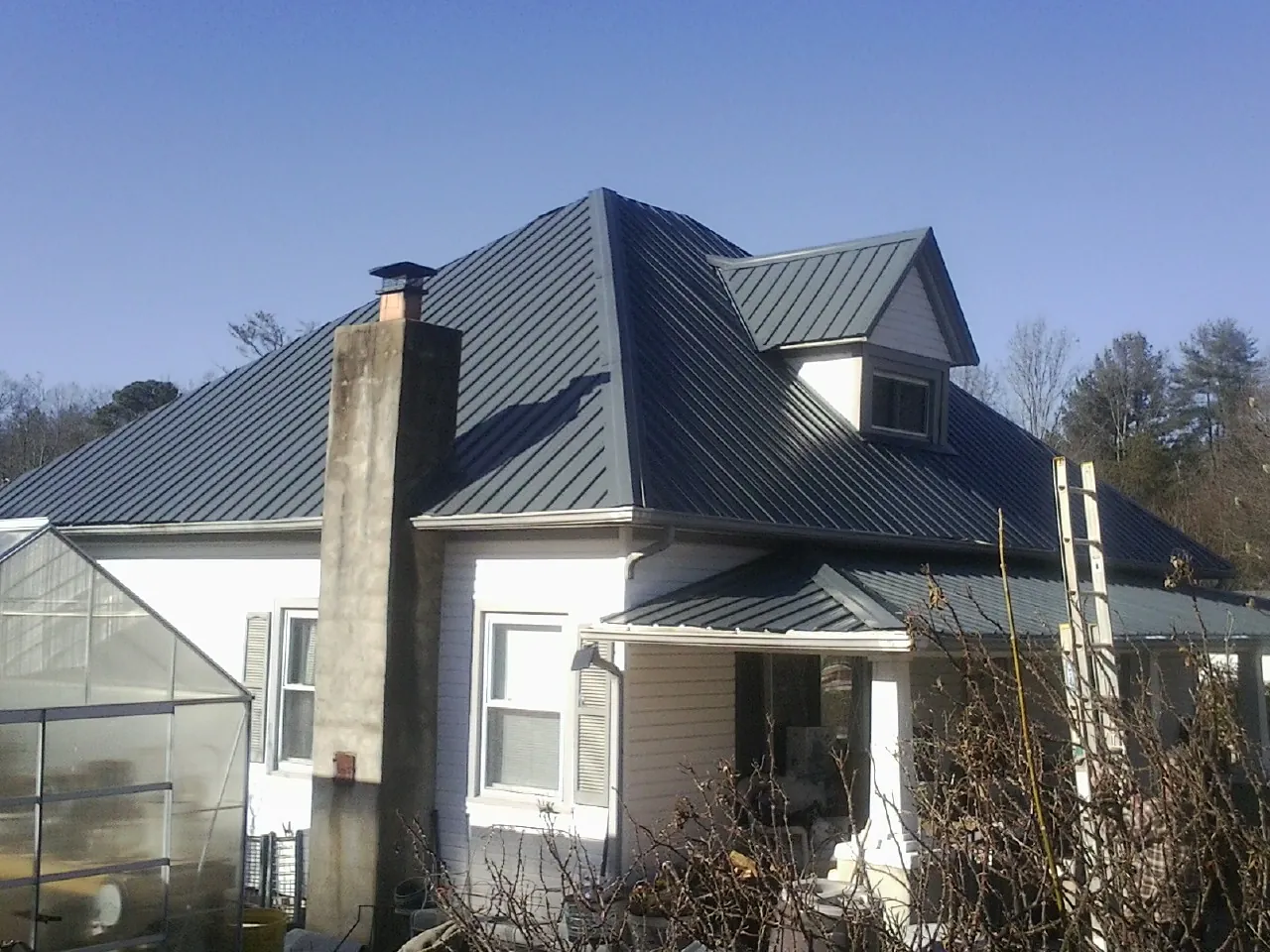 Dark blue standing seam metal roof on a white farmhouse with dormer — Slate & Tile Roof Repair by Roofing Brothers in Cohoes