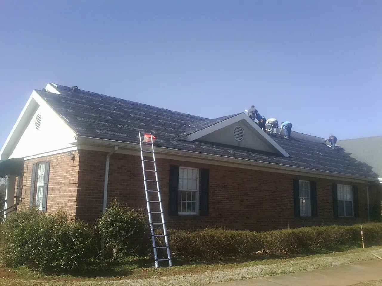 Crew tearing shingles off a brick ranch roof with a ladder set — Metal Roof Repair work by our crew in Cohoes
