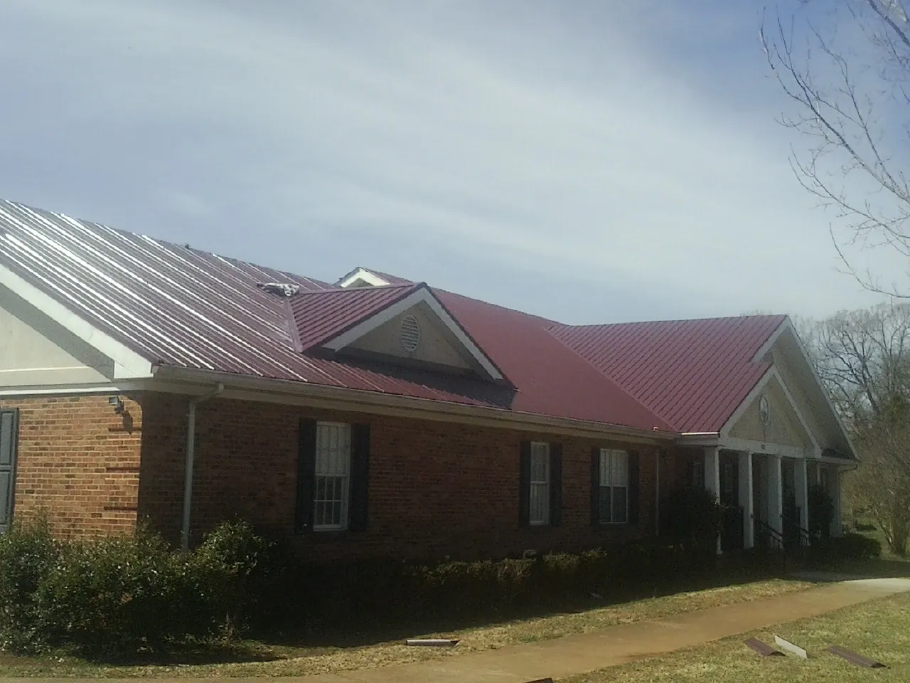 Red metal roof with gabled entries on a long brick building, from a Hail Damage Roof Repair job in Cohoes