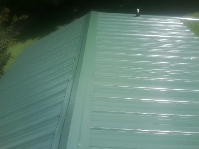 New green metal panels meeting at the ridge of a roof — Flat Roof Repair work by our crew in Cohoes