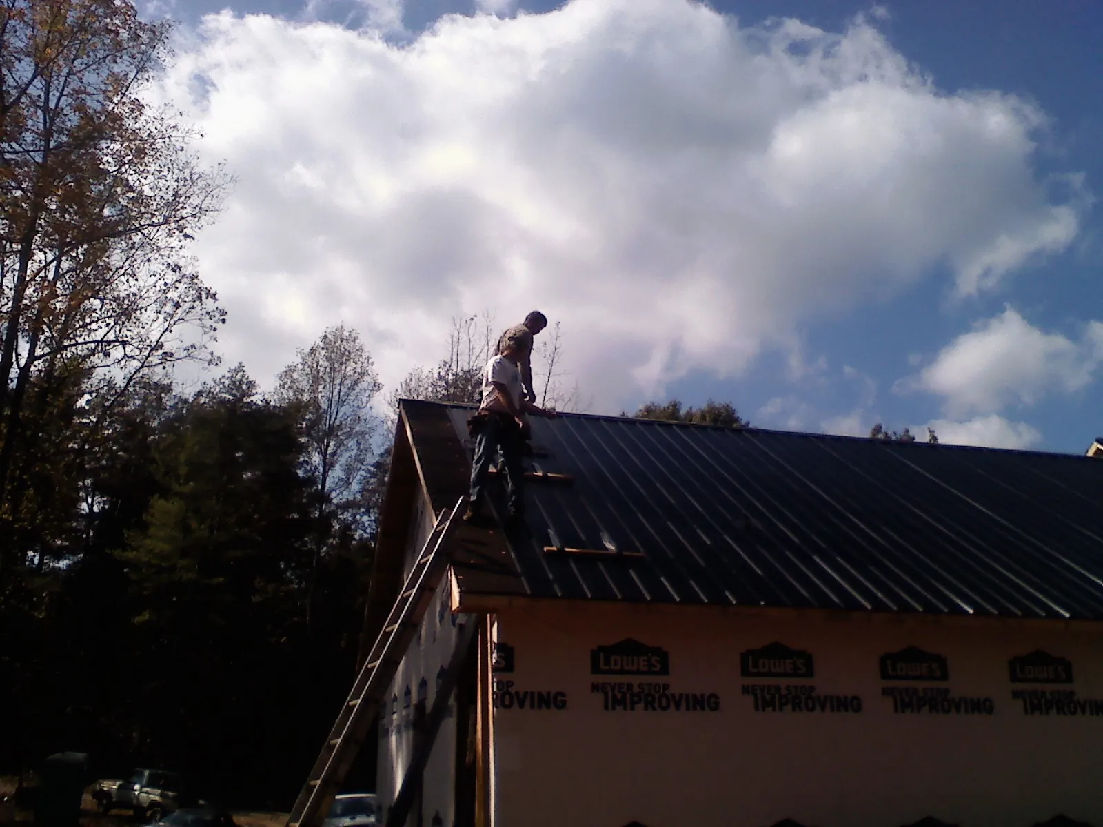 Roofer fastening dark metal panels high against a cloudy sky, from a Roof Inspection job in Cohoes