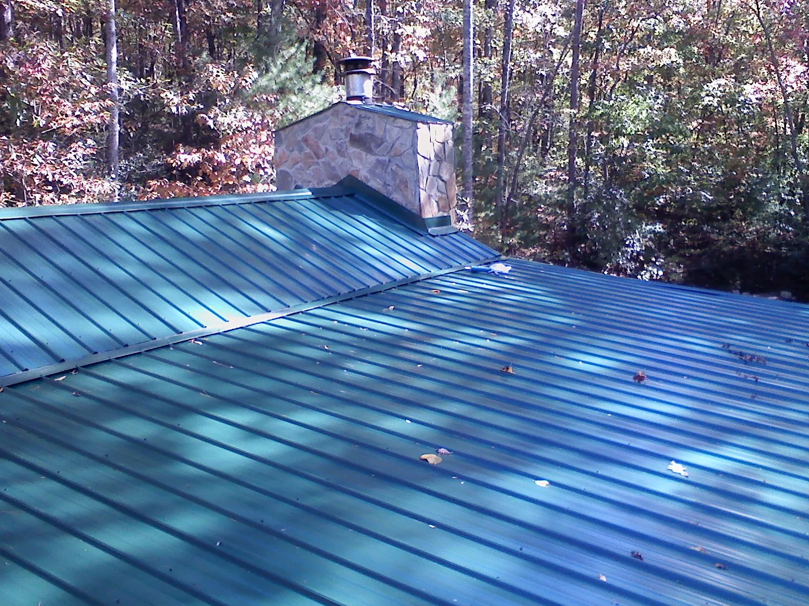 New green metal roof and stone chimney surrounded by autumn woods in Cohoes
