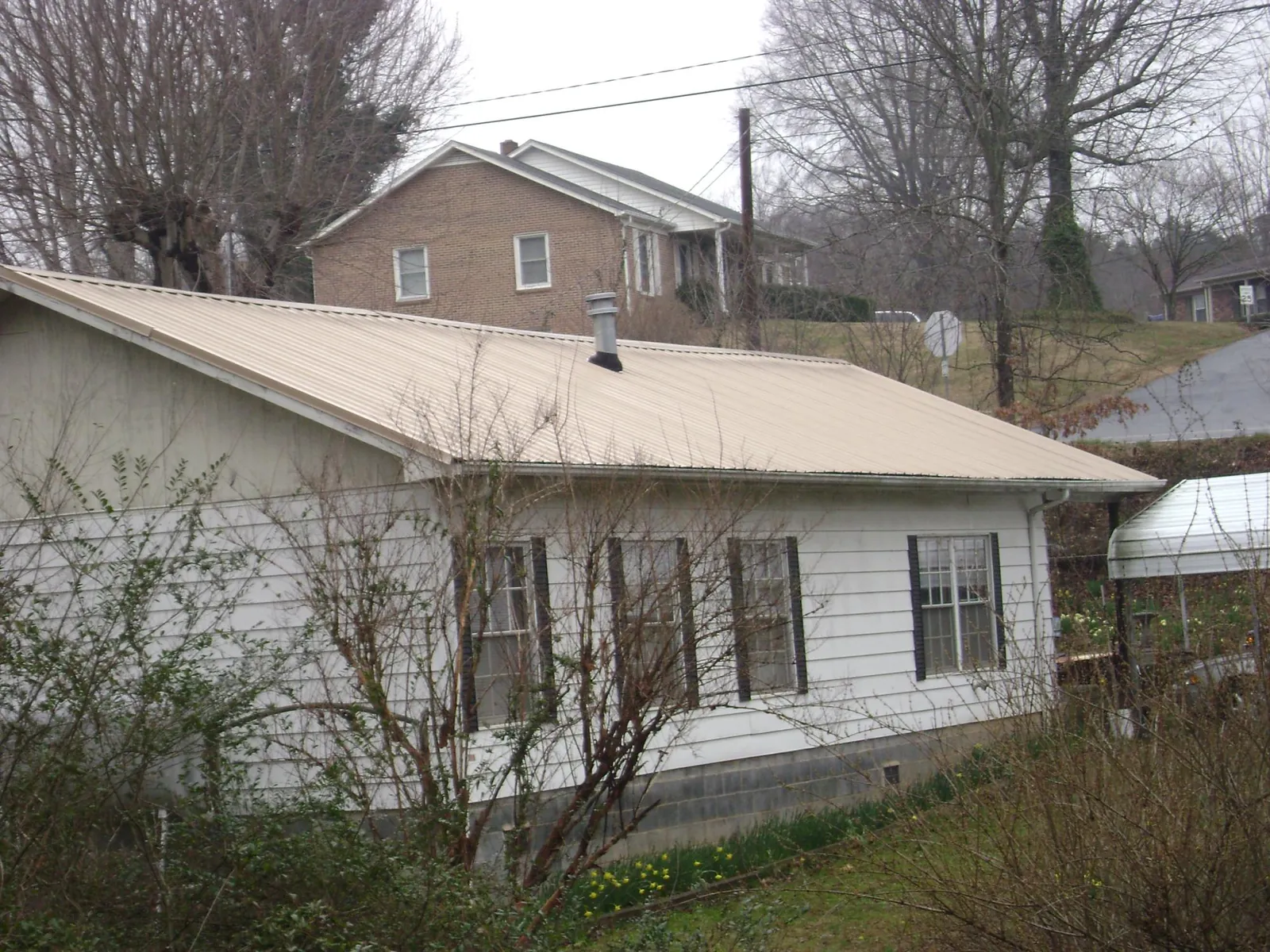 Tan metal roof on a white sided house set into a hillside — Commercial Roofing by Roofing Brothers in Cohoes